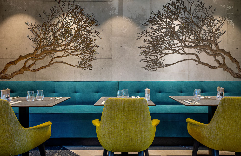 Restaurant au mur en béton décoré de branches d'arbre imprimées, banquette turquoise
