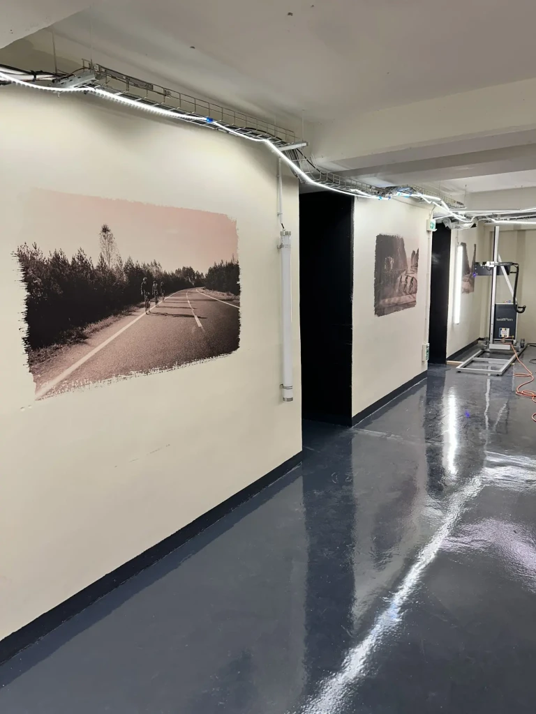 Couloir du parking à vélo avec deux visuels de cyclistes sur route imprimés sur les murs, imprimante Wallpen au fond